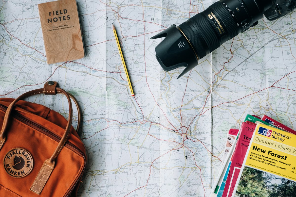 A map laid out with a camera, a notebook and a backpack while planning a trip